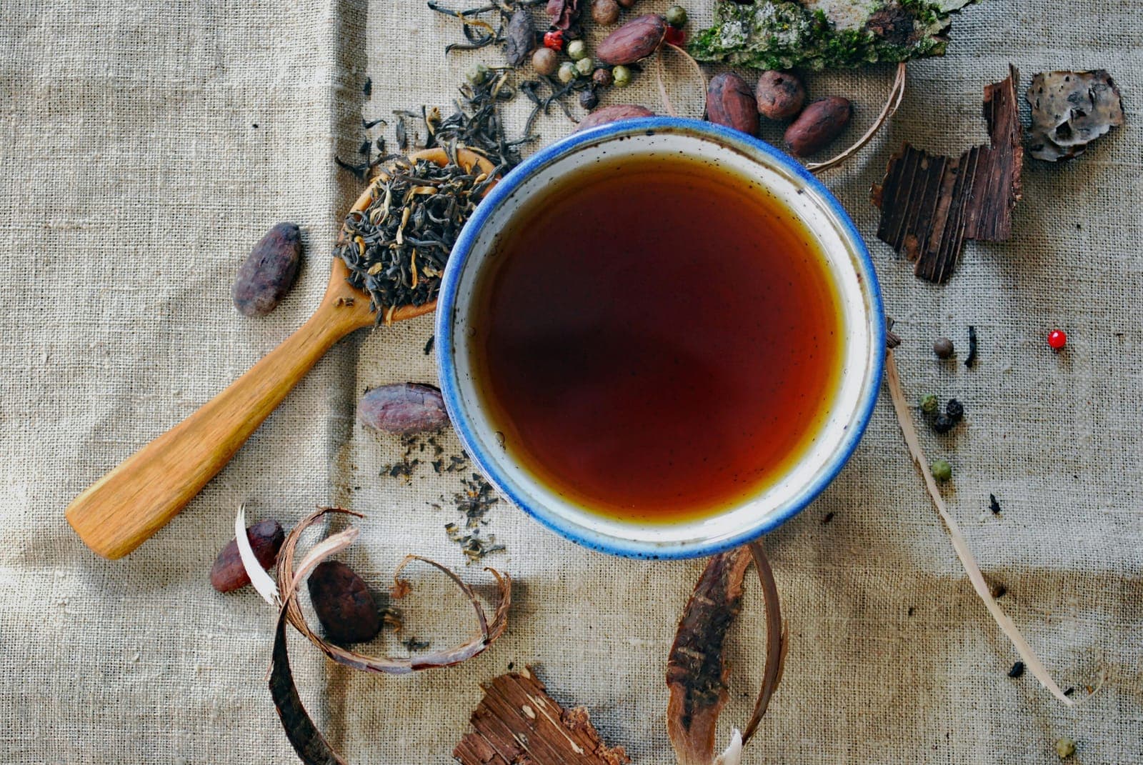 Amber tea in an enamel cup on linen, with loose leaves, bark, and spices