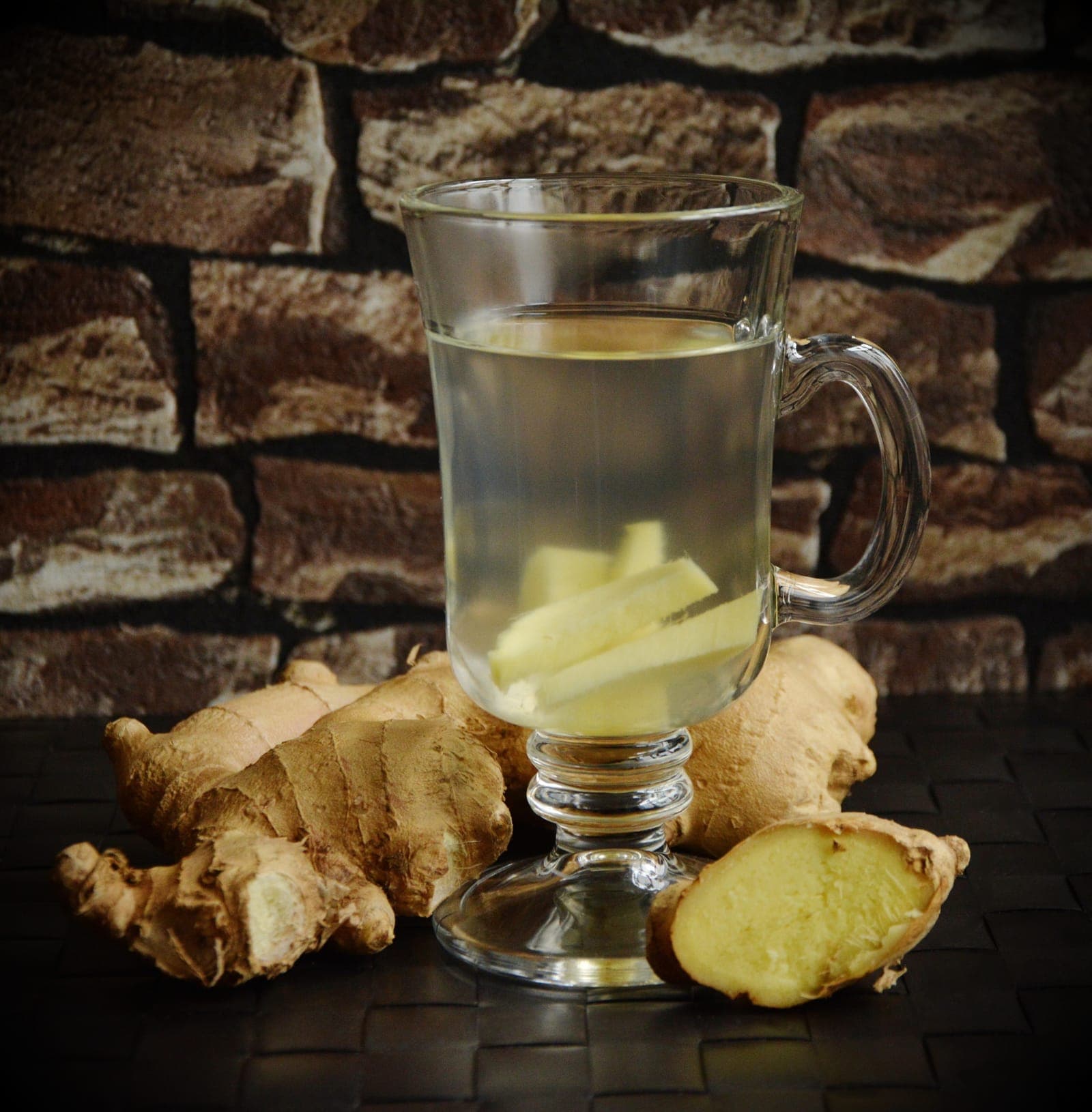 Ginger tea in a glass mug beside fresh ginger root