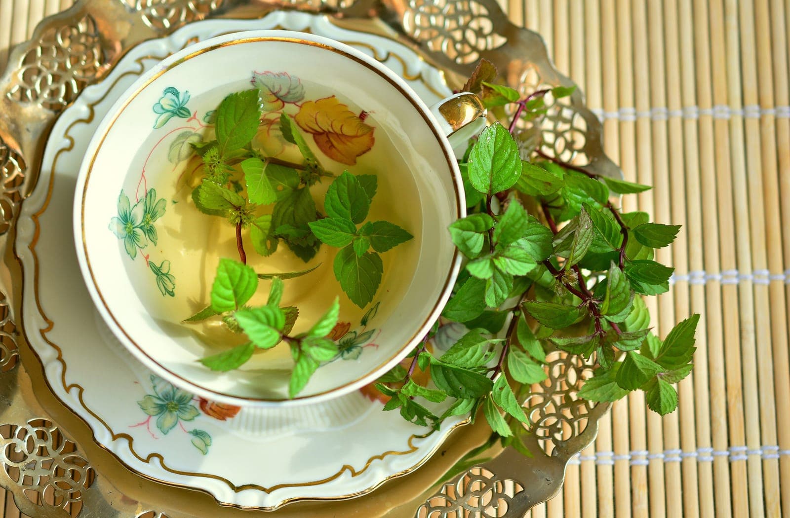 Fresh mint leaves steeping in a porcelain teacup on a woven mat
